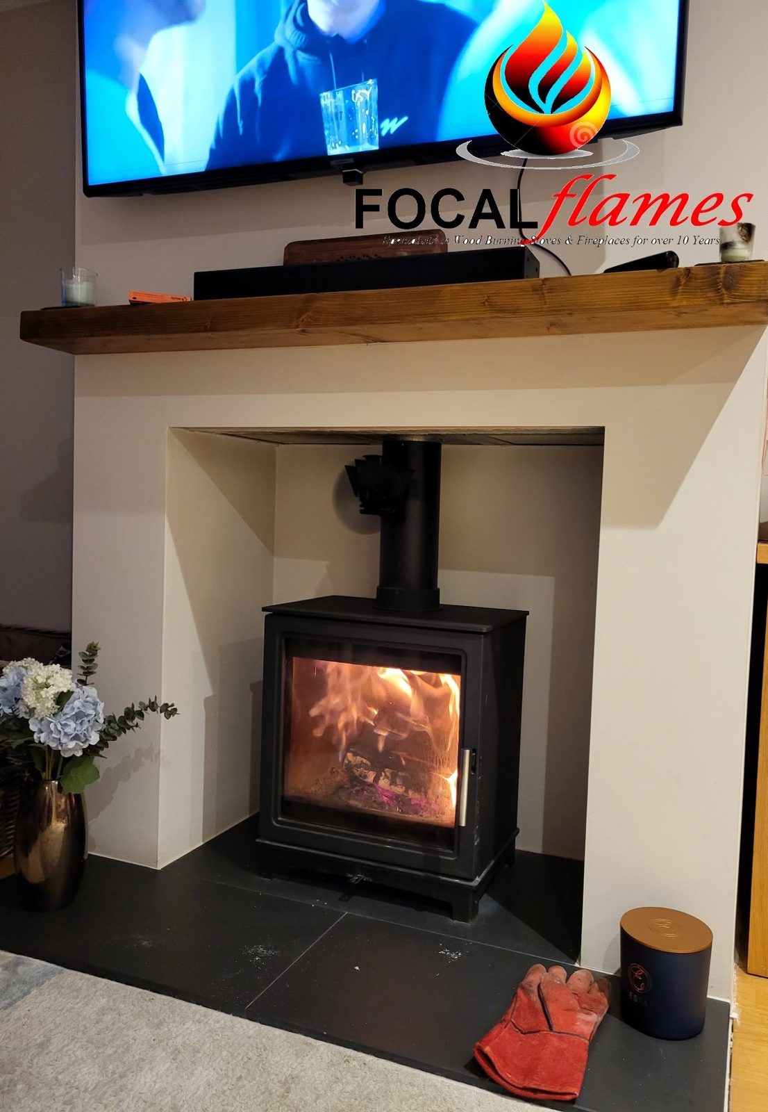 A wood burner on a slate hearth under an oak beam, television above