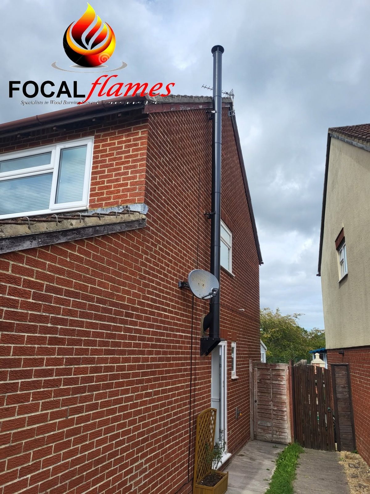 A black twin wall flue running up the outside of a brick house