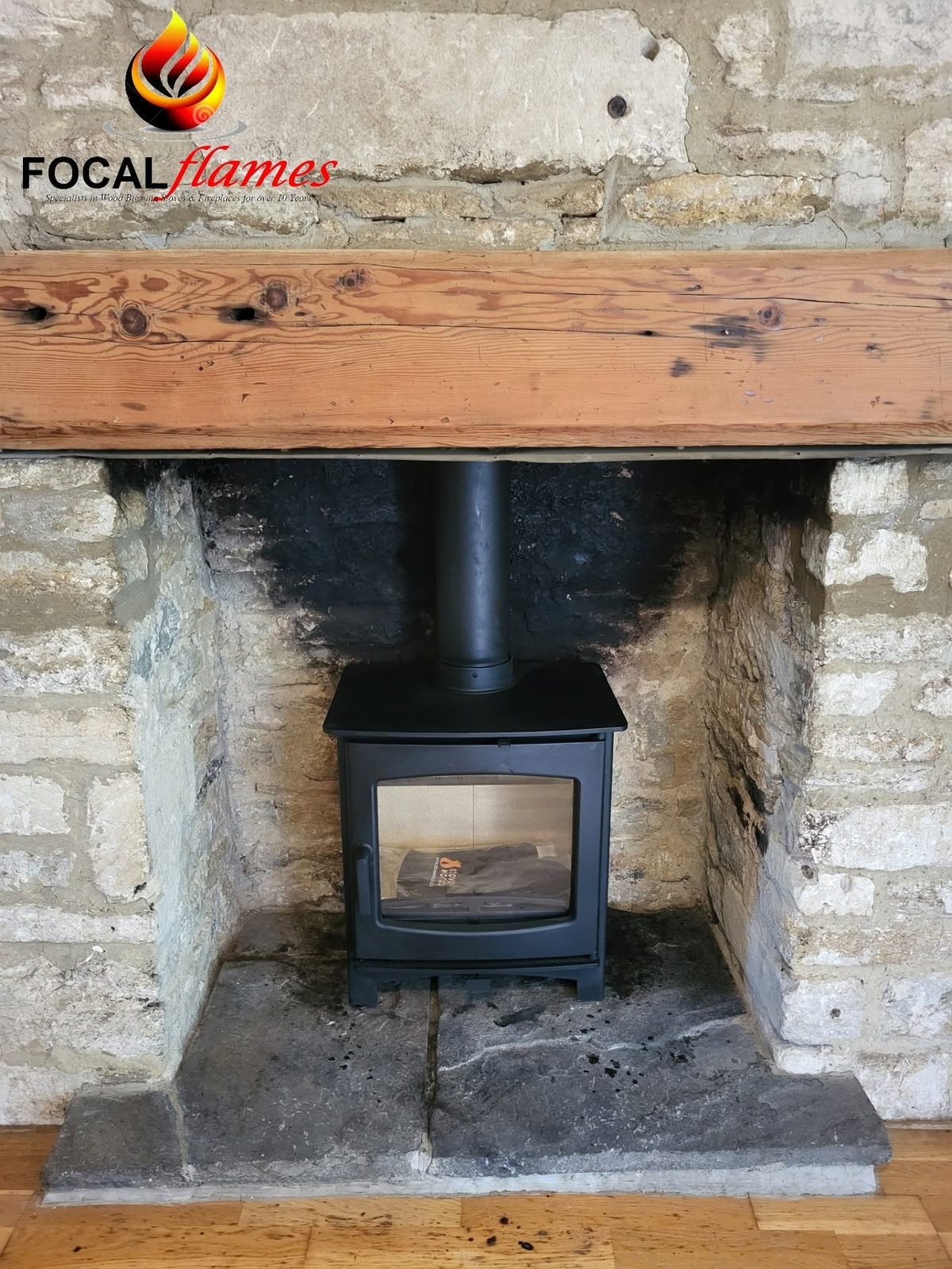 A black stove in a rustic stone recess under an old timber beam