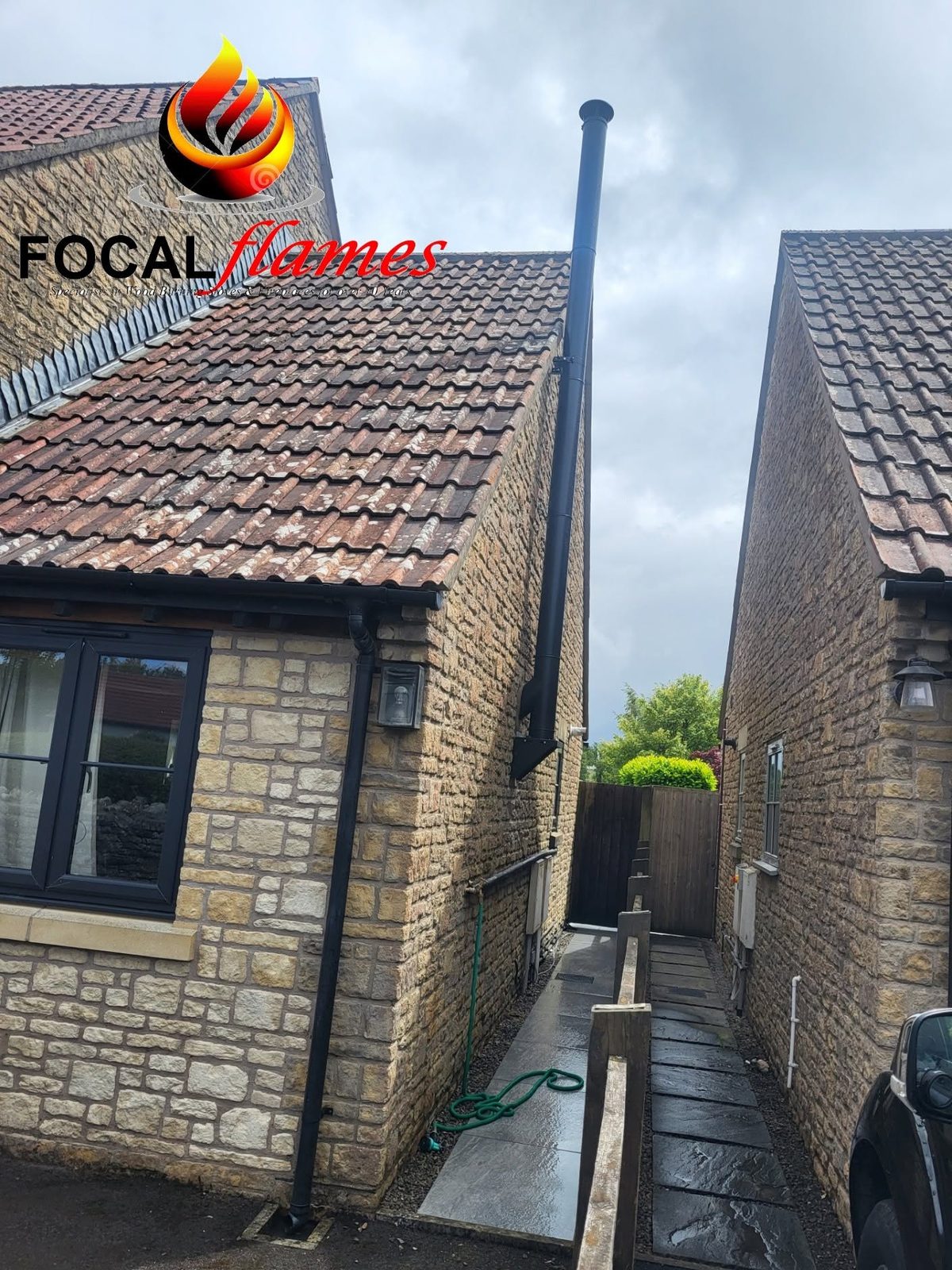 A twin wall flue rising past the roof of a stone cottage extension